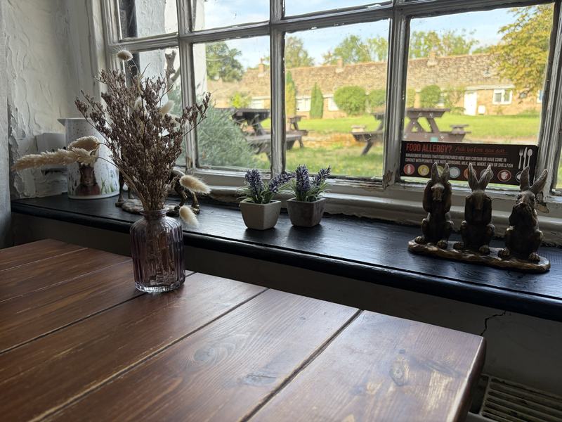 A table by the window with dried flowers and brass hares, looking out to the garden